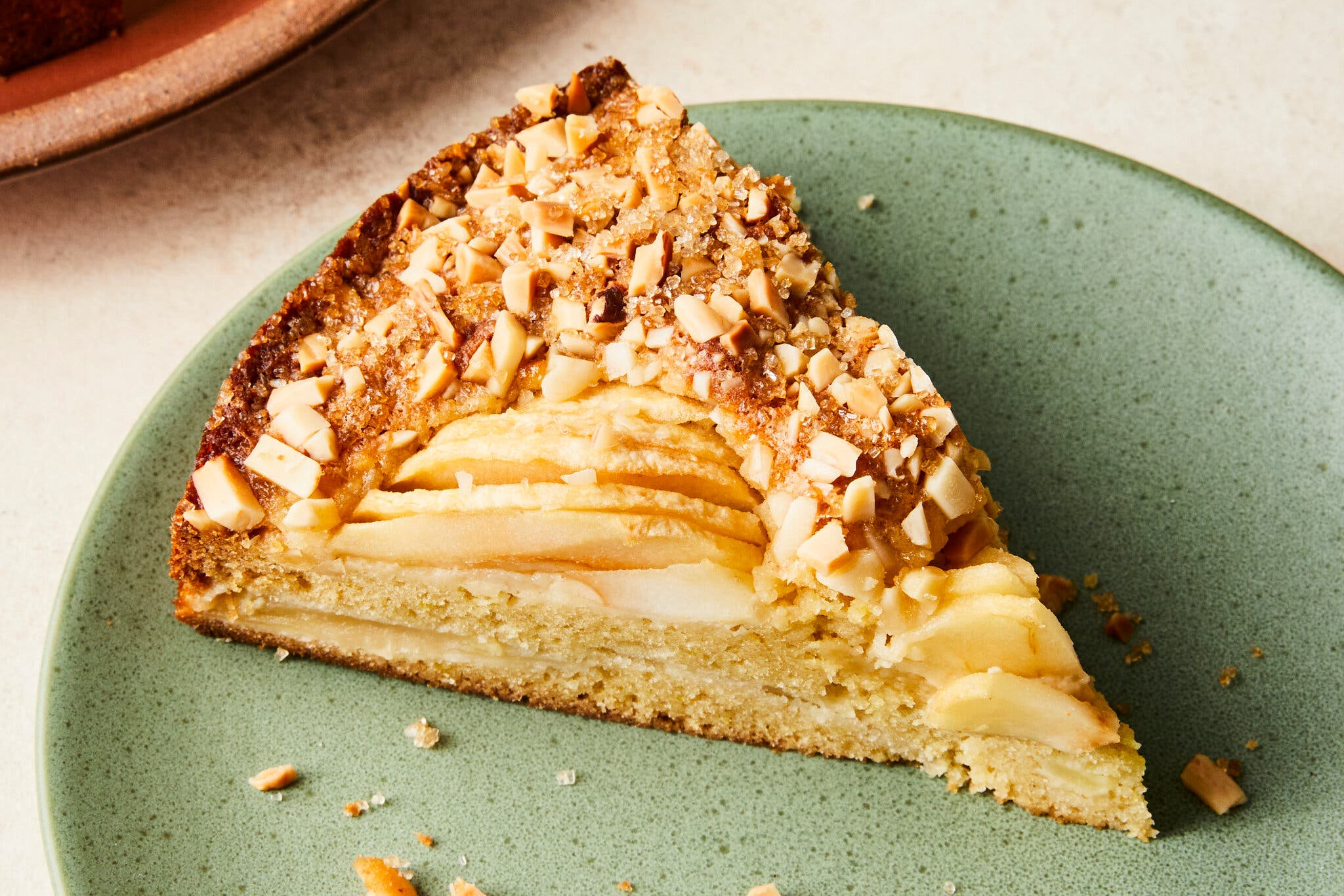 A slice of cake topped with apples and nuts is photographed at an angle.