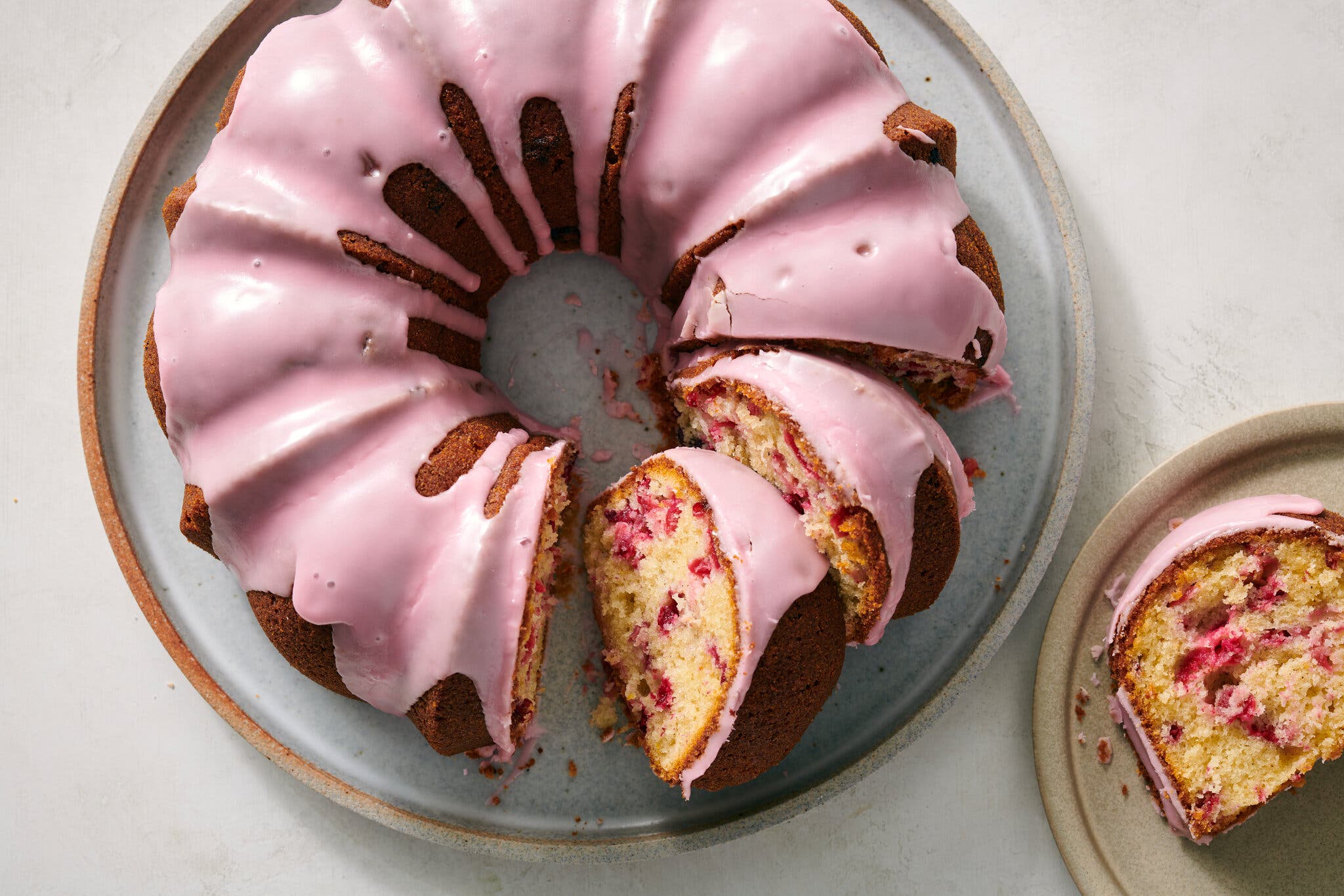 An overhead image of a pink glazed Bundt cake with some slices taken out to reveal some cranberry inside.