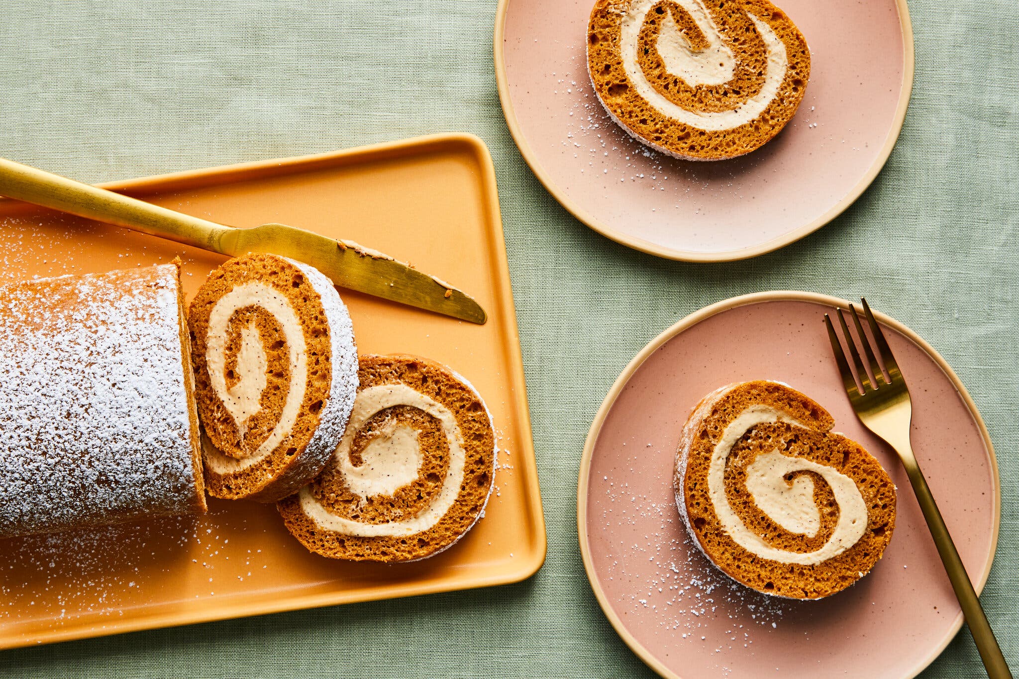 An overhead image of a swirled pumpkin roll on a platter, next to two slices.
