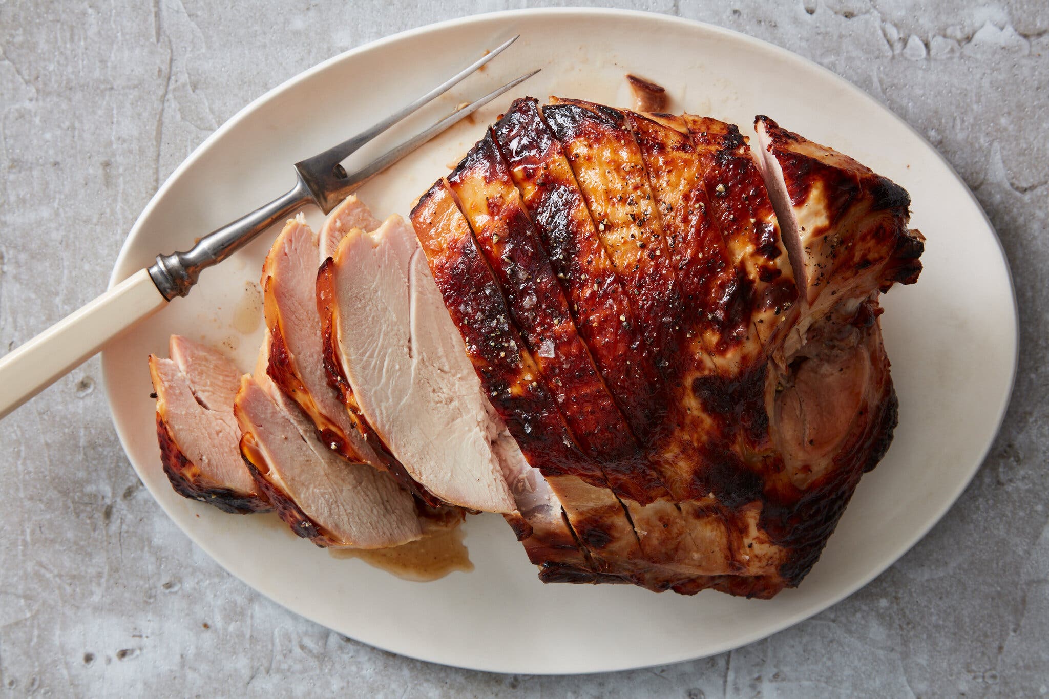 An overhead shot of a sliced buttermilk-brined turkey breast on a white plate. A two-pronged fork sits at the top left corner.