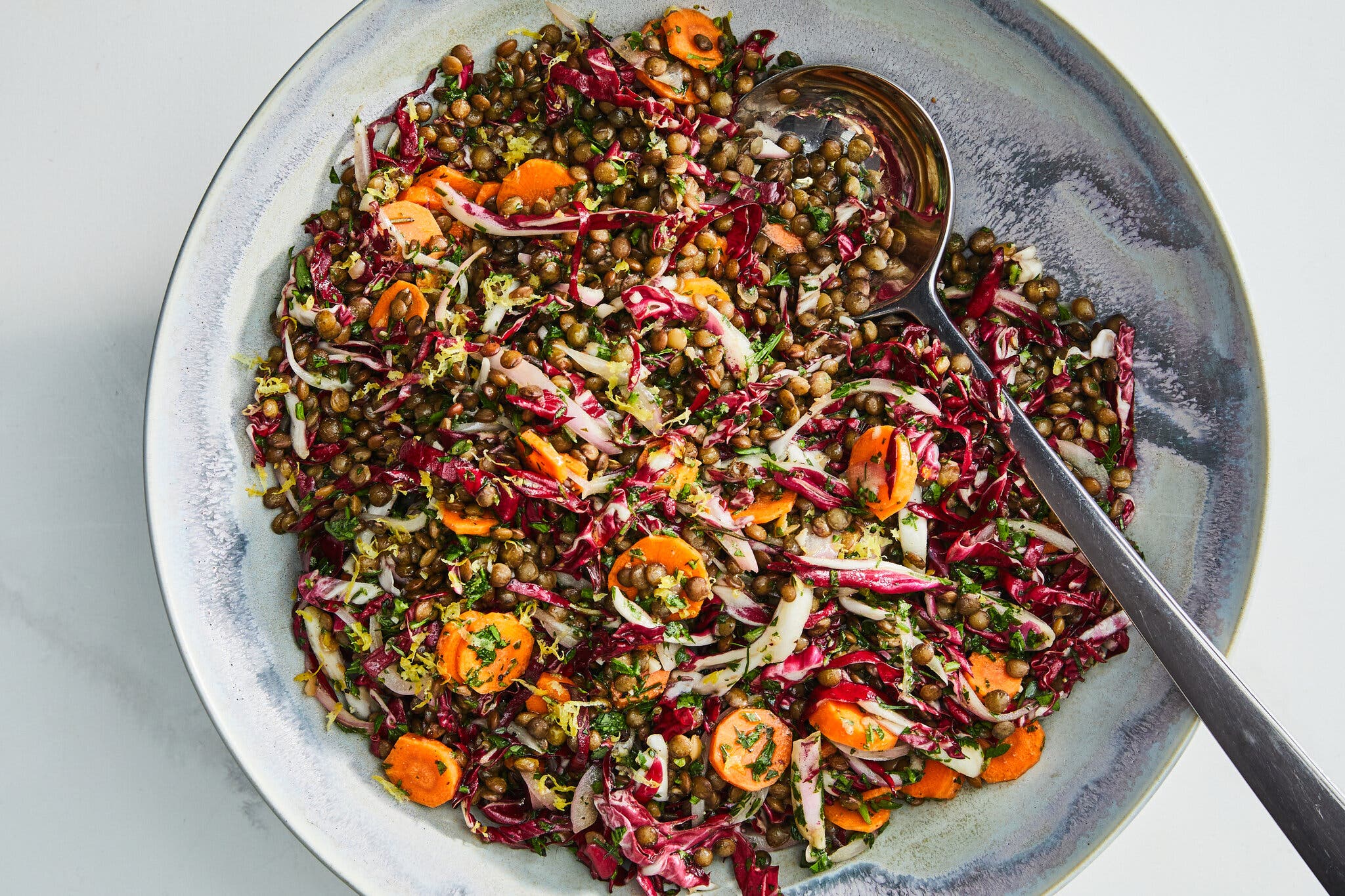 An overhead shot of French lentil salad. A spoon sits on the right side of the bowl.