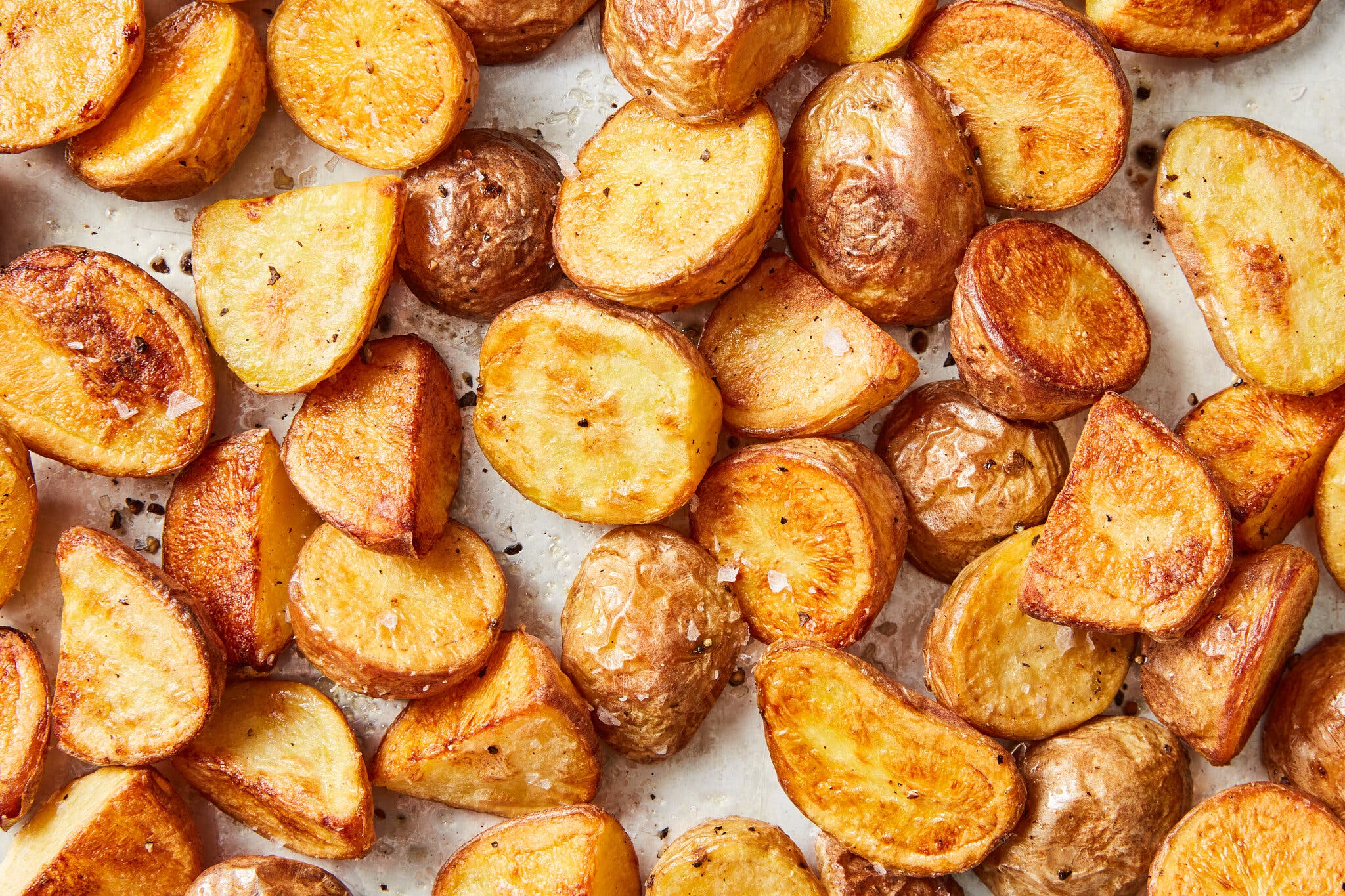 A close-up shot of roasted potatoes sprinkled with salt and black pepper.
