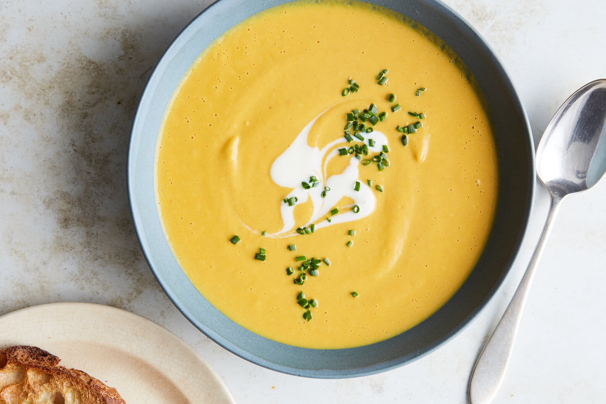 An overhead shot of a blue bowl of spicy peanut and pumpkin soup. A spoon sits next to right side of the bowl.