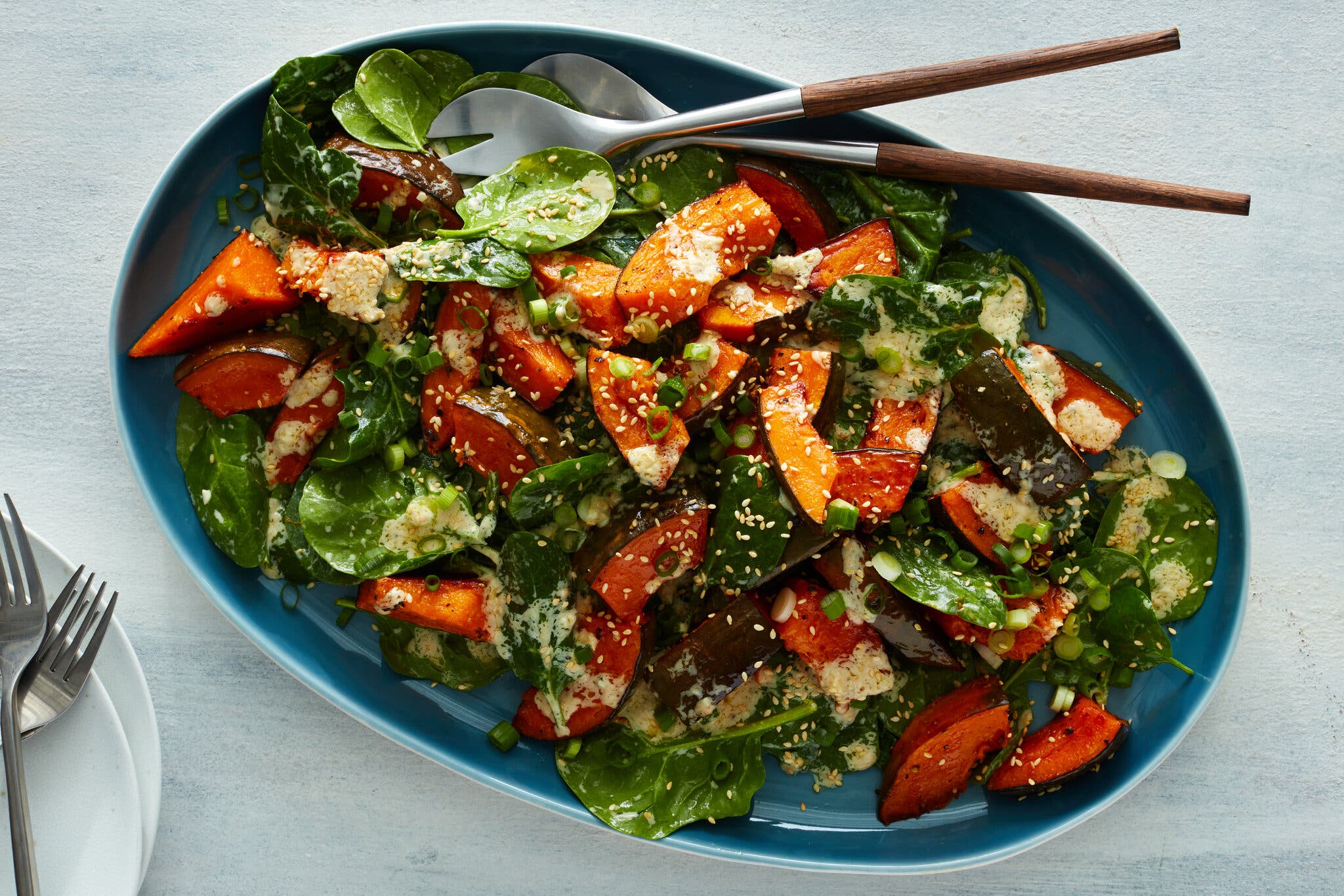 An overhead shot of a blue oblong plate filled with squash and spinach salad with sesame vinaigrette.
