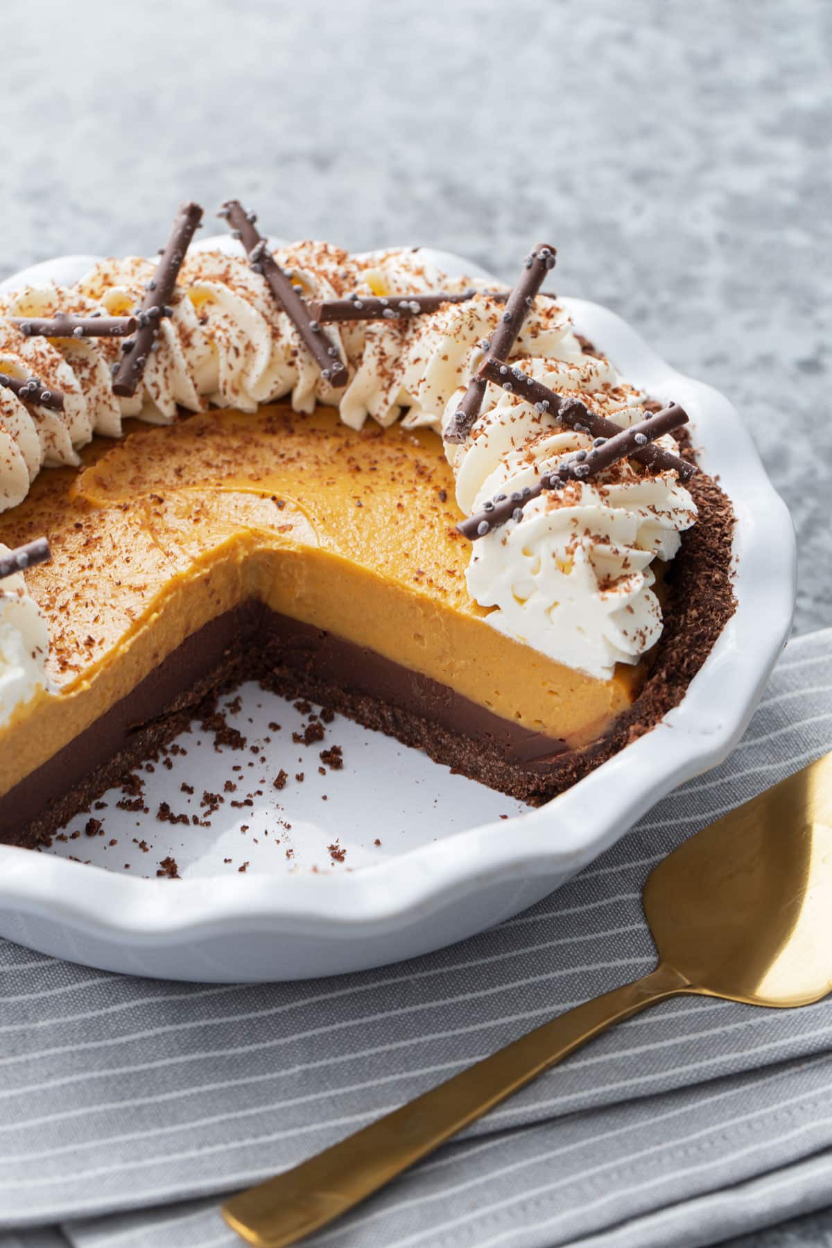 White ceramic pie pan with Black Bottom Pumpkin Cream Pie, a few slices removed to show the distinct layers of chocolate ganache and pumpkin cream.